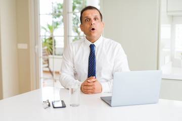 Middle age business man working with computer laptop afraid and shocked with surprise expression, fear and excited face.