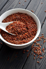red rice in a ceramic bowl with spoon against dark wooden background