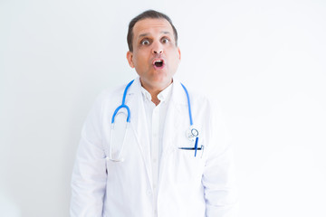 Fototapeta premium Middle age doctor man wearing stethoscope and medical coat over white background afraid and shocked with surprise expression, fear and excited face.