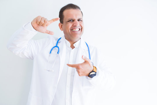 Middle age doctor man wearing stethoscope and medical coat over white background smiling making frame with hands and fingers with happy face. Creativity and photography concept.