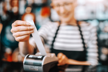 Close up of smiling Caucasian female worker with short blonde hair and eyeglasses using cash register while standing in bicycle store. - obrazy, fototapety, plakaty