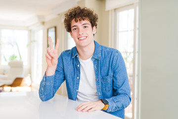 Fototapeta premium Young handsome man wearing casual denim jacket at home smiling with happy face winking at the camera doing victory sign. Number two.