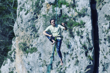 A man is walking along a stretched sling. Highline in the mountains. Man catches balance. Performance of a tightrope walker in nature. Highliner on the background of valley.
