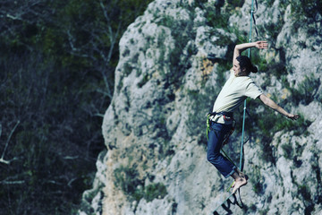A man is walking along a stretched sling. Highline in the mountains. Man catches balance. Performance of a tightrope walker in nature. Highliner on the background of valley.