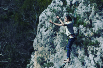 A man is walking along a stretched sling. Highline in the mountains. Man catches balance. Performance of a tightrope walker in nature. Highliner on the background of valley.