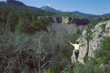 A man is walking along a stretched sling. Highline in the mountains. Man catches balance. Performance of a tightrope walker in nature. Highliner on the background of valley.