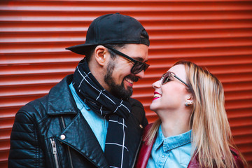 Bearded man and woman in sunglasses have fun over red wall