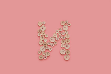 letter of wooden buttons on pink background