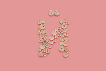 letter of wooden buttons on pink background