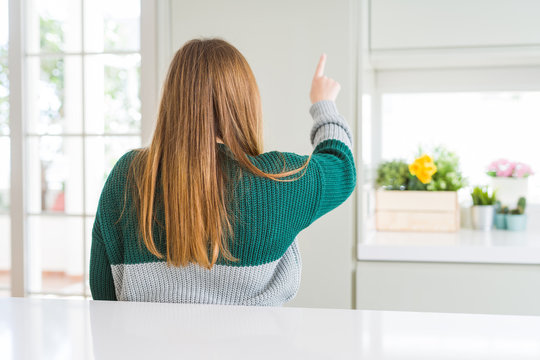 Young beautiful plus size woman wearing casual striped sweater Posing backwards pointing ahead with finger hand