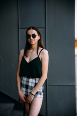 Sexy girl near a dark wall in a T-shirt, sunglasses and short shorts