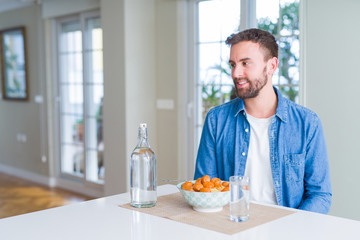 Handsome man eating pasta with meatballs and tomato sauce at home looking away to side with smile on face, natural expression. Laughing confident.