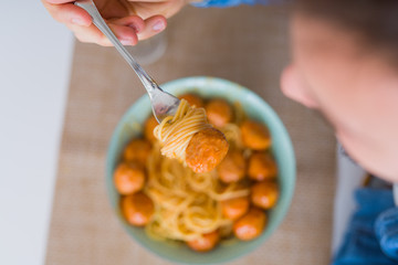Close up of man eating a plate of pasta with meatballs and tomato sauce