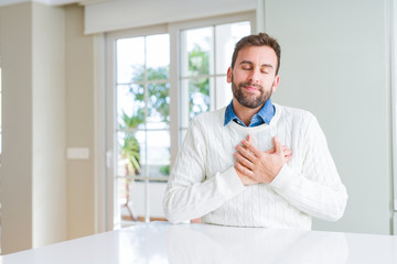 Handsome man wearing casual sweater smiling with hands on chest with closed eyes and grateful...