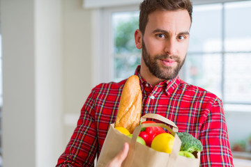 Handsome man holding paper bag full of fresh groceries at home