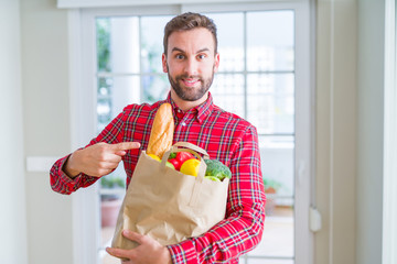 Handsome man holding groceries bag very happy pointing with hand and finger