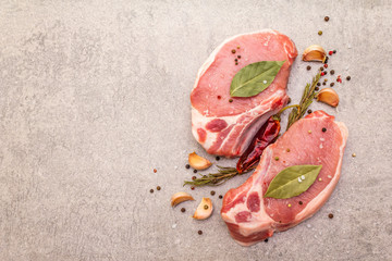 Raw pork steak with spices and dried herbs. Salt, garlic, hot pepper, rosemary, bay leaf on a stone background, top view.
