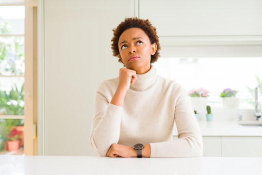 Young beautiful african american woman at home with hand on chin thinking about question, pensive expression. Smiling with thoughtful face. Doubt concept.