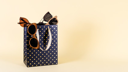 Wooden sunglasses of different design in shopping bags on yellow background. Sale concept. Copy space