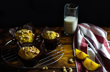 Tasty fresh lemon muffins with nuts and glass of milk on a wooden table. Dark food photography
