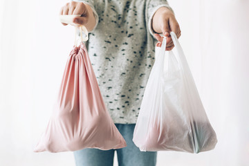 Woman holding in one hand groceries in reusable eco bag and in other vegetables in plastic polyethylene bag. Choose plastic free items. Ban single use plastic. Zero Waste shopping concept.