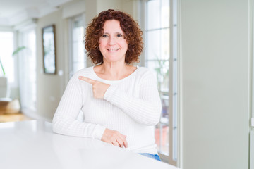 Beautiful senior woman wearing white sweater cheerful with a smile of face pointing with hand and finger up to the side with happy and natural expression on face