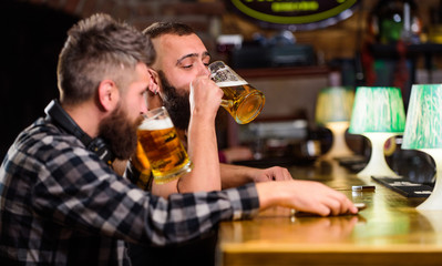 Hipster brutal man drinking beer with friend at bar counter. Men drunk relaxing having fun. Alcohol drinks. Friends relaxing in pub with beer. Refreshing beer concept. Men drinking beer together