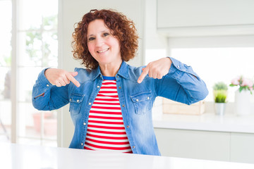 Middle age senior woman with curly hair wearing denim jacket at home looking confident with smile on face, pointing oneself with fingers proud and happy.