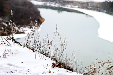 Winter landscape, dry grass covered with white frost on the precipice of a wide river.