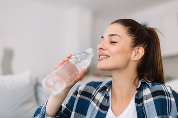Girl holding a bottle of water. Smiling girl drinking water.