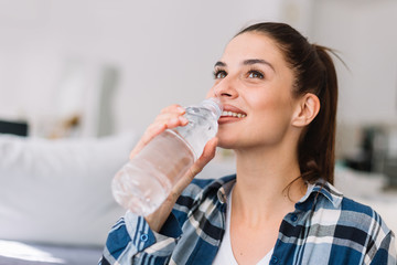 Girl holding a bottle of water. Smiling girl drinking water.