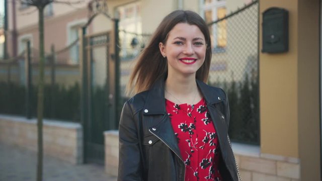 Pure young woman with charming smile walking through street, sitting in car. Driver's seat. Portrait of pleasant-looking girl in long red dress. Outside. New  vehicle.