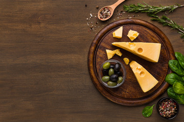 Cheese, olives and fresh herbs on wooden background.