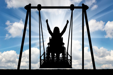 Silhouette of a happy woman is a disabled person in a wheelchair on an adaptive swing for disabled...