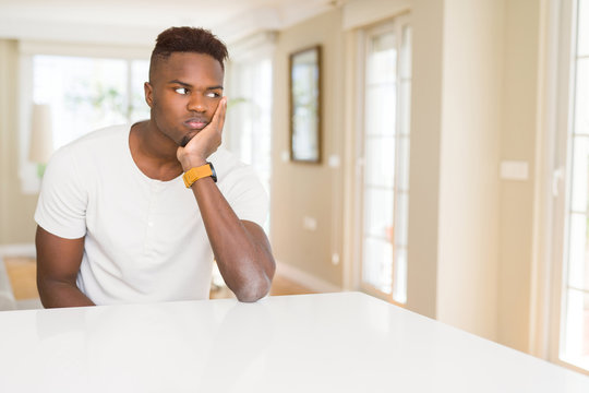 Handsome african american man on white table at home thinking looking tired and bored with depression problems with crossed arms.