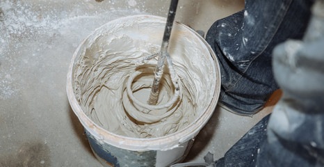 Man is mixing spackling paste putty in the bucket. Grind of wall. Maintenance repair works renovation in the flat. Restoration indoors. Concrete background.