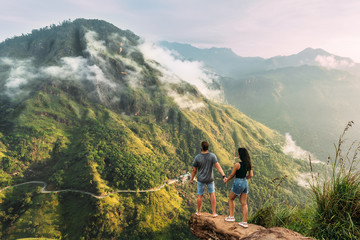 The couple greets the sunrise in the mountains. Man and woman in the mountains. Man and woman holding hands. The couple travels around Asia. Travel to Sri Lanka. Serpentine in the mountains. Honeymoon - obrazy, fototapety, plakaty