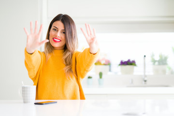 Young beautiful woman drinking a cup of coffee at home showing and pointing up with fingers number nine while smiling confident and happy.