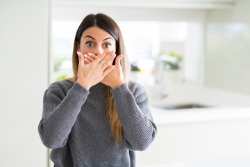 Young beautiful woman wearing winter sweater at home shocked covering mouth with hands for mistake. Secret concept.