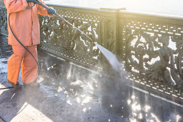 Worker cleaning driveway with gasoline high pressure washer splashing the dirt, railings, bumpers...