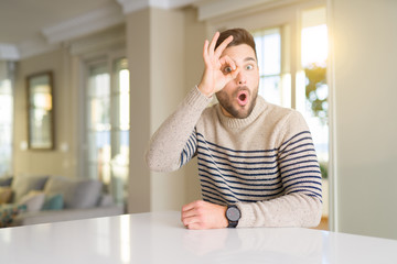 Young handsome man at home doing ok gesture shocked with surprised face, eye looking through fingers. Unbelieving expression.