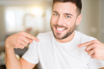 Young handsome man wearing casual white t-shirt at home looking confident with smile on face, pointing oneself with fingers proud and happy.