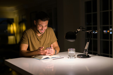 Young handsome man studying at home , using smartphone, looking at the phone smiling