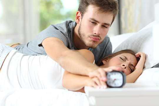 Sleepy couple waking up turning off alarm clock in the bed