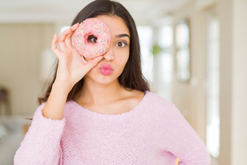 Beautiful young woman looking through pink donut on the eye sending a kiss