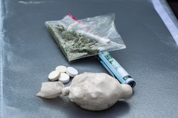 drugs: white powder in a package, twisted bill, grass with a joint and a few white tablets lie on a gray folder