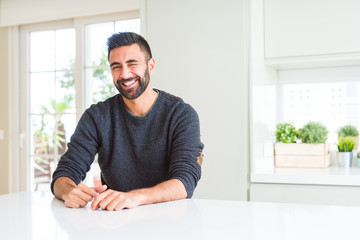 Handsome hispanic man wearing casual sweater at home winking looking at the camera with sexy expression, cheerful and happy face.