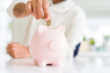 Obraz na płótnie Canvas Man putting a coin inside of piggy bank saving for investment