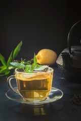 Cup of tea, melissa and black teapot on dark. Chinese tea concept.