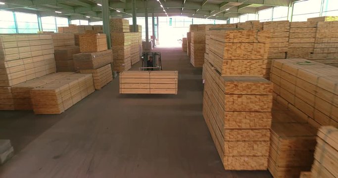A large warehouse of timber materials. A forklift carries a wooden beam through the warehouse. Neatly stacked wooden bar in a sawmill warehouse